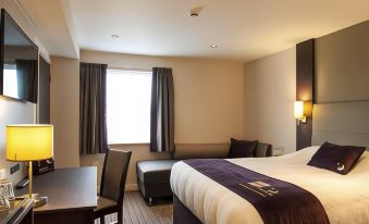 a hotel room with a bed , couch , and dining table , along with a window and light on the ceiling at Premier Inn Trowbridge