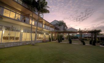 a large building with a balcony and palm trees is surrounded by green grass and palm trees at Mercure Clear Mountain Lodge