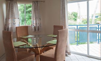 a dining room with a round glass table and chairs , surrounded by windows that offer a view of the outdoors at Marina Terraces Port Douglas