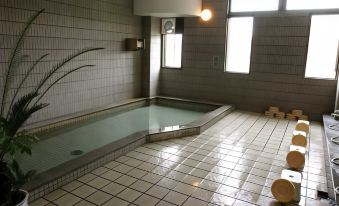 an empty indoor swimming pool with white tiles , surrounded by a bathroom with a window at Jukeiso