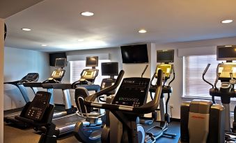 a well - equipped gym with various exercise equipment , including treadmills and stationary bikes , set against a backdrop of windows at Penn Harris Hotel Harrisburg, Trademark by Wyndham