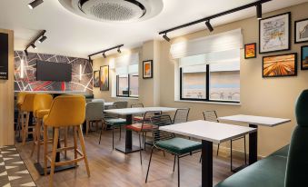a modern , open - concept dining area with multiple tables and chairs , surrounded by windows and a ceiling fan at Super 8 by Wyndham Chester East