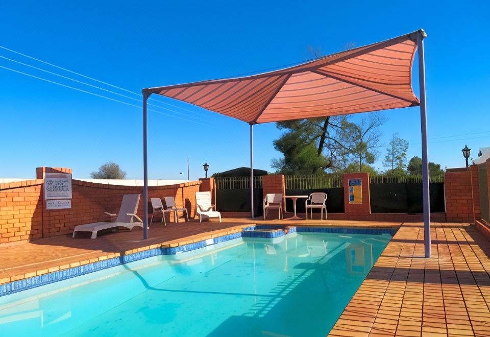 a large swimming pool with a wooden deck and lounge chairs under an umbrella , surrounded by a brick building at Comfort Inn Bishops Lodge