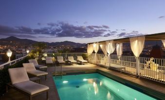 a rooftop pool surrounded by lounge chairs , with a view of the city in the background at Splendid Hotel & Spa Nice