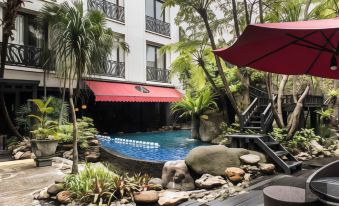 a luxurious outdoor pool area with a red umbrella , rocks , and greenery surrounding a building at Amaroossa Hotel Bandung Indonesia