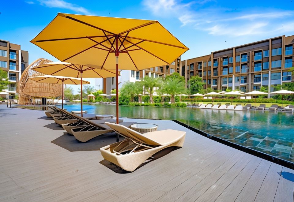 a swimming pool with umbrellas and lounge chairs , surrounded by buildings and trees , under a clear blue sky at Divalux Resort and Spa Bangkok, Suvarnabhumi Airport-Free Shuttle