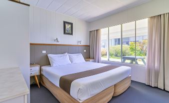 a large bed with white linens and a brown blanket is in a room with wooden furniture at Aloha Apartments