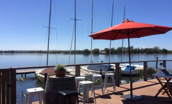 a wooden dock with several sailboats docked in the water , surrounded by tables and chairs for outdoor dining at Lake Wendouree Luxury Apartments