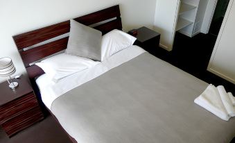 a bed with white sheets and pillows is situated next to a nightstand in a bedroom at Monterey Apartments Moranbah