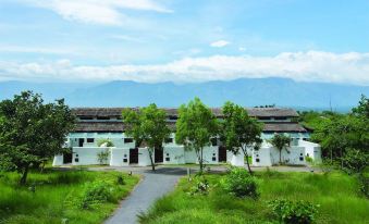 a long white building surrounded by green grass and trees , with mountains in the background at The Serai Bandipur