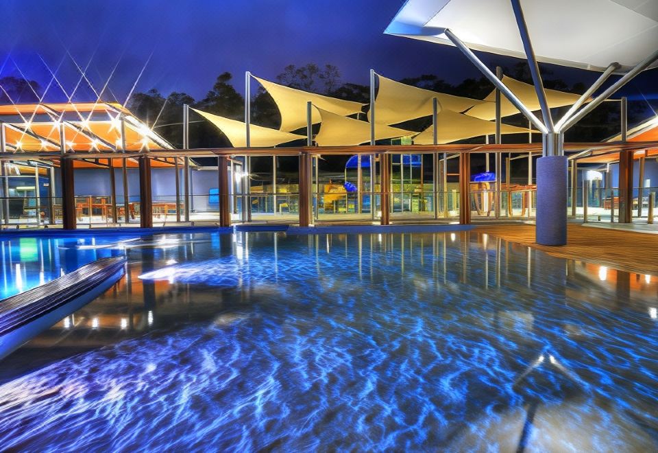a large swimming pool with a unique geometric design , surrounded by tall buildings and lit up at night at Ingenia Holidays Lake Conjola