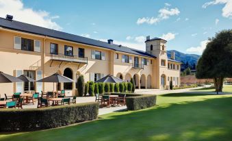 a large yellow building with a balcony overlooks a green lawn with several tables and chairs at Hanmer Springs Hotel