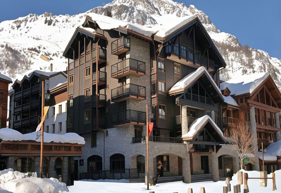 a snow - covered ski resort with multiple buildings , including a large apartment complex with balconies and a mountain in the background at Avenue Lodge Hotel & Spa