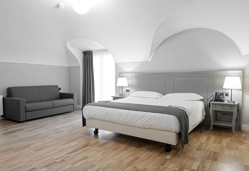 a modern bedroom with a large bed , white walls , and hardwood floors , accompanied by a couch and lamp at Hotel de Ville