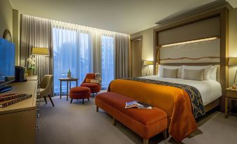 a modern hotel room with a large bed , orange bench , and two nightstands , all set against a backdrop of a city skyline at Clayton Hotel Chiswick
