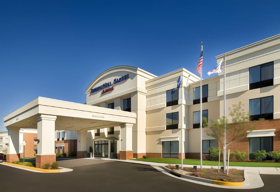 a hampton inn hotel with an american flag flying in front of it , surrounded by cars and trees at SpringHill Suites Alexandria