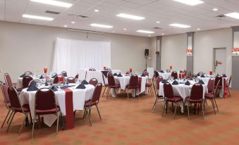 a large , well - lit room with multiple tables set for dining and chairs arranged for a meeting or event at Ramada by Wyndham New Iberia
