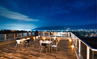 a rooftop terrace with wooden flooring , white tables and chairs , and a city view at night at Fuefukigawa Onsen Zabou