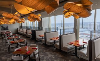 a restaurant with white booths and chairs , red tablecloths , and orange hanging lights , overlooking the ocean at DoubleTree by Hilton Cedar Rapids Convention Complex