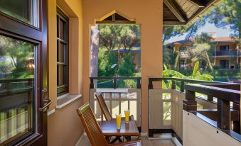 a wooden chair and table are set up on a balcony overlooking a lush green garden at Aquaworld Belek