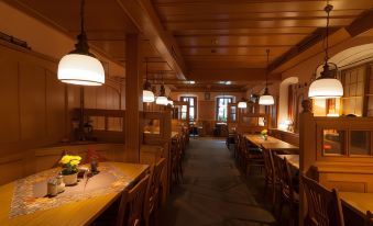 a long dining room with wooden tables and chairs , pendant lights hanging from the ceiling , and a few potted plants on the table at Akzent Hotel Schranne