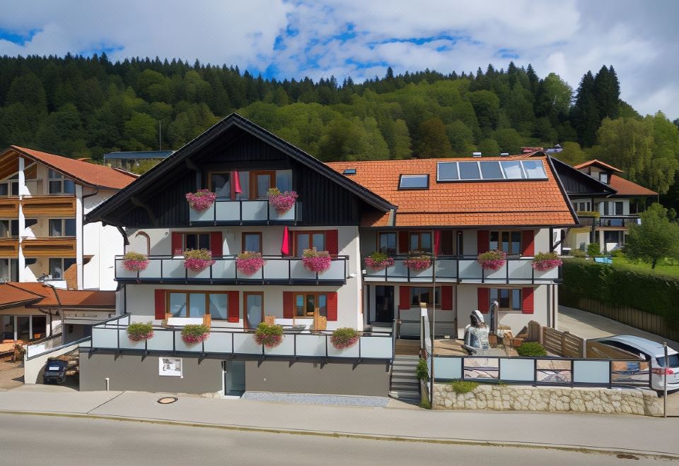 a large , two - story building with red shutters and balconies , situated in a mountainous area under a clear blue sky at Hotel Haus am See