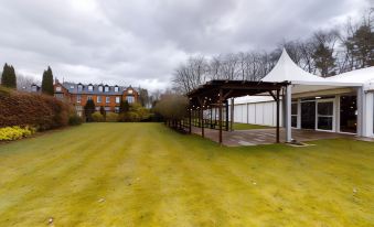 a large grassy area with a wooden shelter and a white tent in the background at Nunsmere Hall Hotel