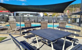 a group of picnic tables and benches situated next to a swimming pool , with a clear blue sky in the background at Zig ZAG Motel & Apartments