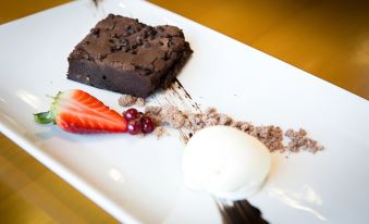 a white plate with a piece of chocolate cake , topped with a scoop of ice cream and strawberries , placed on a dining table at Ramada Plaza by Wyndham Wrexham