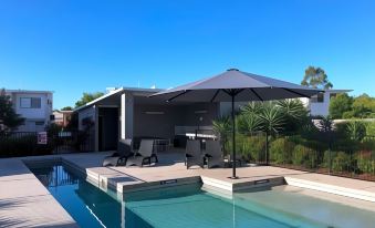 a large swimming pool with lounge chairs and an umbrella is surrounded by a modern house at Direct Collective - Breeze on Brightwater