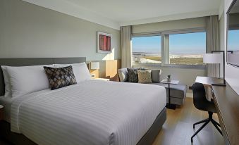 a modern hotel room with a large window offering a view of the ocean , featuring a bed , desk , and comfortable seating area at Athens Marriott Hotel