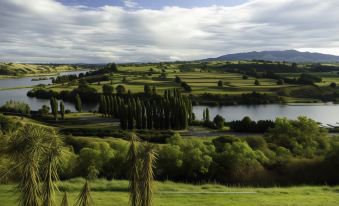 a serene landscape with rolling hills , green fields , and a lake surrounded by trees , under a cloudy sky at Lake Karapiro Lodge