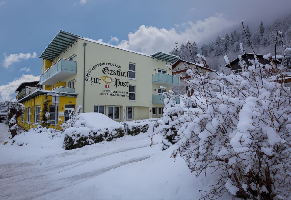 a snowy day in a mountainous area , with a hotel building covered in snow and adorned with balconies at Gasthof Zur Post