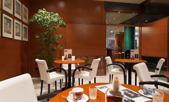 a modern coffee shop with wooden tables and chairs , white chairs , and a green plant at Hotel Firenze