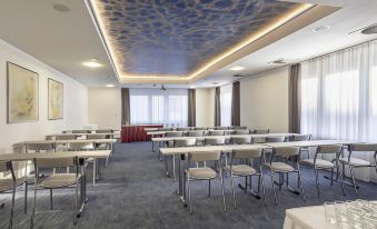 a conference room with rows of tables and chairs , a blue ceiling , and large windows at Hotel Continental