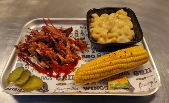 a plate of food with meat , corn on the cob , and macaroni and cheese is displayed at Coach House Hotel