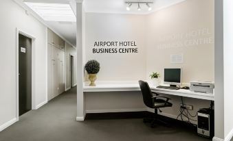 an airport hotel business centre with a desk and chairs , as well as a potted plant at Airport Hotel Sydney
