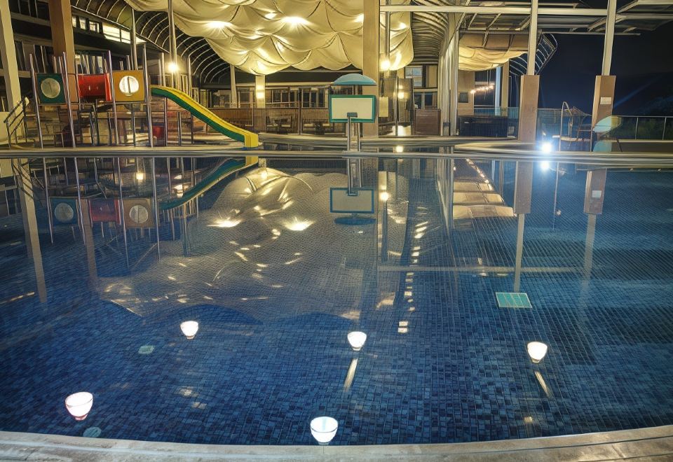 a modern indoor swimming pool with a blue tiled floor , surrounded by white walls and glass windows at Hotel Cianjur Cipanas