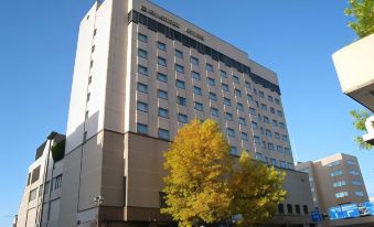 a tall , beige building with a gray facade and many windows , standing next to a tree in front of it at Hotel Metropolitan Morioka New Wing