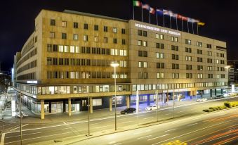 a large hotel building at night , with the exterior lit up and flags flying from its balconies at Steigenberger Graf Zeppelin
