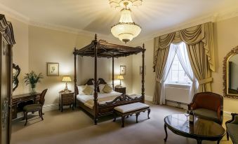 a large bedroom with a wooden canopy bed , a chair , and a chandelier hanging from the ceiling at Doxford Hall Hotel and Spa