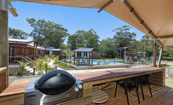 a backyard with a barbecue grill and a swimming pool surrounded by wooden decking , chairs , and umbrellas at Reflections Jimmys Beach - Holiday Park