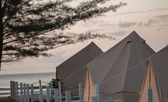 two beige tents set up on a wooden platform , surrounded by trees and the ocean at Cabana Retreat - Glamping
