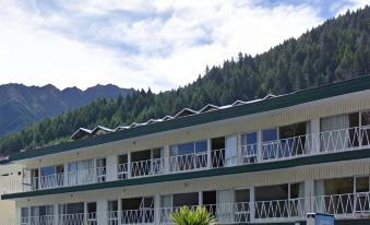 a modern building with multiple floors , balconies , and greenery , set against a backdrop of mountains and clear skies at Lakeside Motel