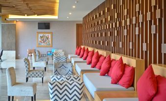 a modern lounge area with multiple couches and chairs , along with red pillows and a unique geometric patterned wall at FamVida Hotel Lubuklinggau Powered by Archipelago