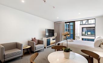 a modern hotel room with a king - sized bed , a television , a dining table , and chairs at Fernz Motel & Apartments Birkenhead