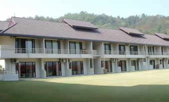 a large white building with multiple floors and balconies , situated in front of a grassy field at DoiTung Lodge