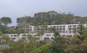 a large white building surrounded by trees , with a view of the ocean in the background at Pacific Bay Resort