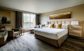 a large bed with white linens and brown headboard is in a room with wooden floors , a window , and a painting on the wall at Forest Park Hotel