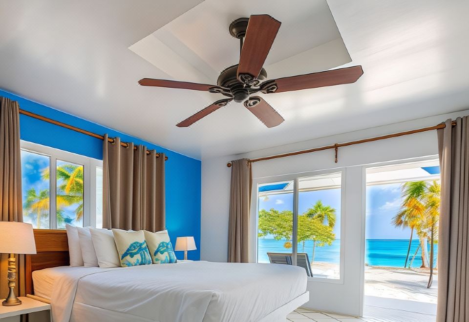 a bedroom with a large bed and a ceiling fan , overlooking the ocean through the windows at Pelican Beach Hotel